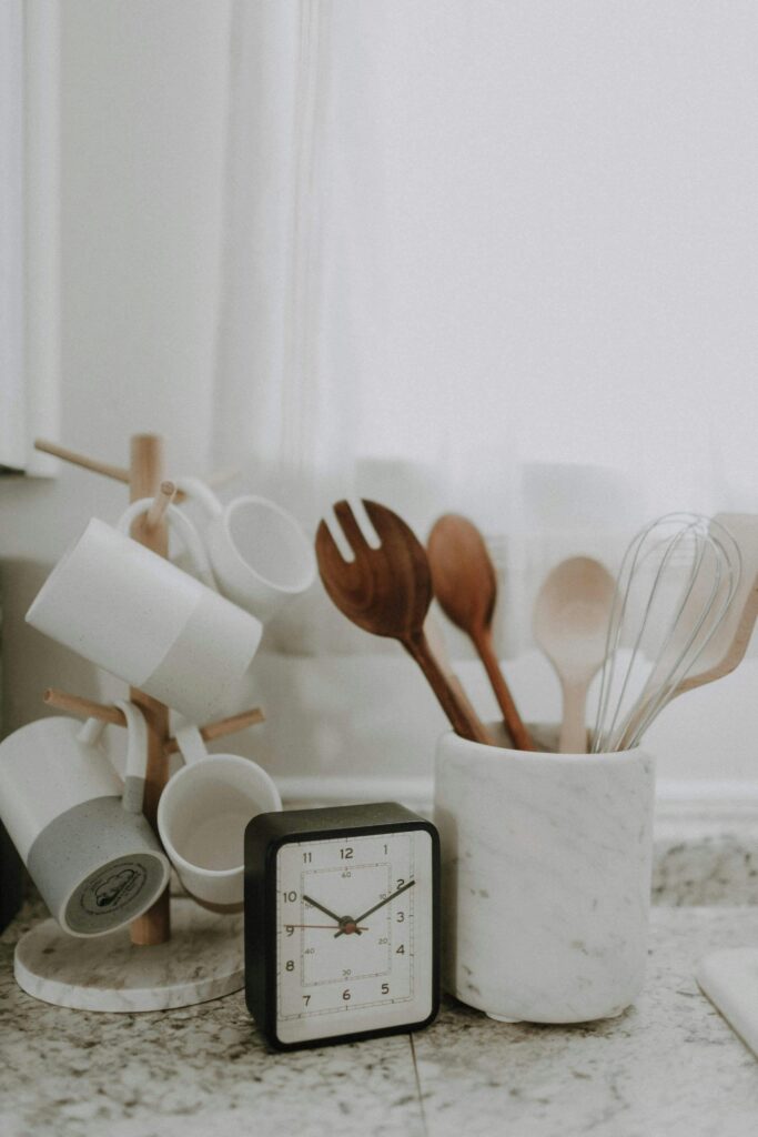 A minimalist kitchen scene featuring utensils, mugs, and a clock on the counter.