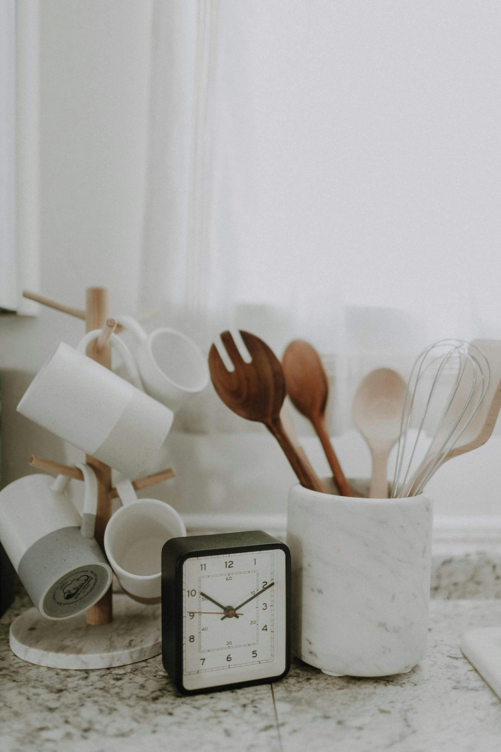 A minimalist kitchen scene featuring utensils, mugs, and a clock on the counter.